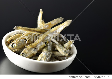 A small plate of boiled dried sardines is photographed against a black background. A small plate of boiled dried sardines is photographed against a black background. 95074506