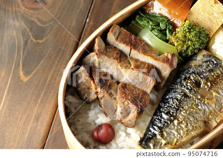 A bird's-eye view of a grilled fish bento box containing pork, potato salad, omelet, etc. 95074716