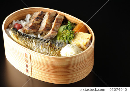 A grilled fish bento box containing pork, potato salad, omelet, etc. is photographed against a black background. A grilled fish bento box containing pork, potato salad, omelet, etc. is photographed against a black background. 95074940