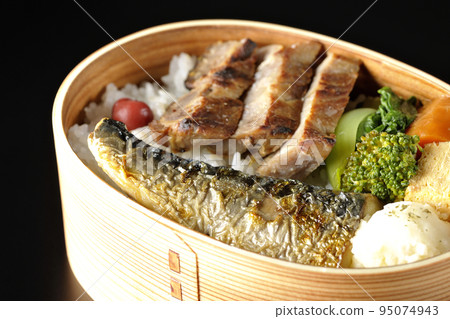 A grilled fish bento box containing pork, potato salad, omelet, etc. is photographed against a black background. 95074943