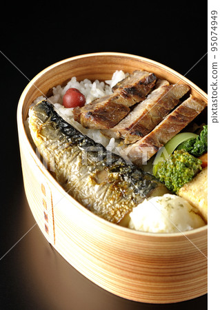 A grilled fish bento box containing pork, potato salad, omelet, etc. is photographed against a black background. A grilled fish bento box containing pork, potato salad, omelet, etc. is photographed against a black background. 95074949
