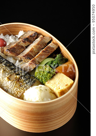 A grilled fish bento box containing pork, potato salad, omelet, etc. is photographed against a black background. A grilled fish bento box containing pork, potato salad, omelet, etc. is photographed against a black background. 95074950