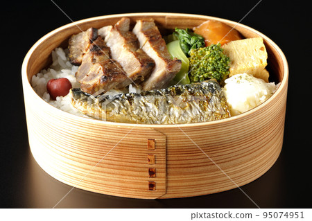 在黑色背景下拍攝了一個烤魚便當盒，裡面有豬肉、土豆沙拉、煎蛋捲等。 95074951