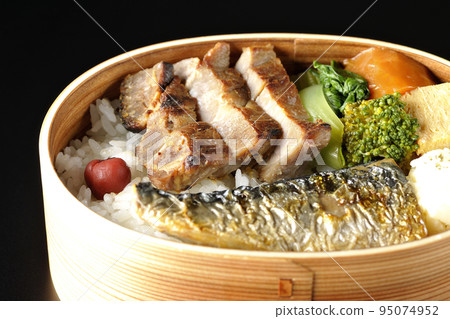 A grilled fish bento box containing pork, potato salad, omelet, etc. is photographed against a black background. A grilled fish bento box containing pork, potato salad, omelet, etc. is photographed against a black background. 95074952