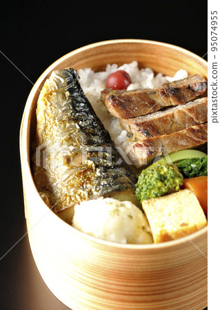 A grilled fish bento box containing pork, potato salad, omelet, etc. is photographed against a black background. A grilled fish bento box containing pork, potato salad, omelet, etc. is photographed against a black background. 95074955