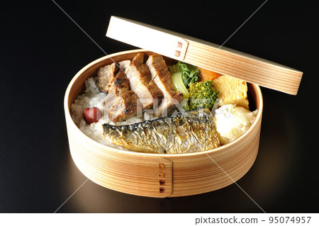 A grilled fish bento box containing pork, potato salad, omelet, etc. is photographed against a black background. 95074957
