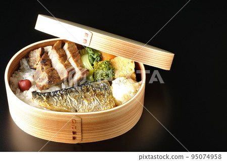 A grilled fish bento box containing pork, potato salad, omelet, etc. is photographed against a black background. A grilled fish bento box containing pork, potato salad, omelet, etc. is photographed against a black background. 95074958