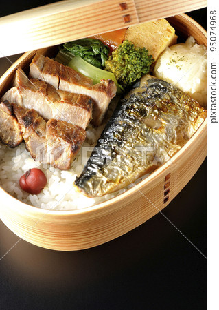 A grilled fish bento box containing pork, potato salad, omelet, etc. is photographed against a black background. A grilled fish bento box containing pork, potato salad, omelet, etc. is photographed against a black background. 95074968