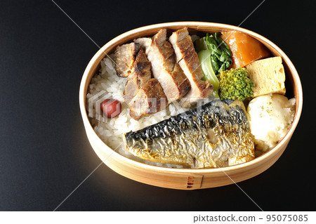 A bird's-eye view of a grilled fish bento box containing pork, potato salad, omelet, etc. in a black background 95075085