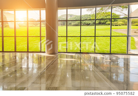 Clean and bright modern interior space in the evening with grass outside the floor-to-ceiling windows Clean and bright modern interior space in the evening with grass outside the floor-to-ceiling windows 95075582