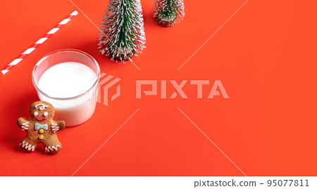 Christmas festive banner with milk glass, gingerbread man, decorative christmas trees on red backdrop. Milk for Santa concept. Holiday greeting card. Copy space for text. Selective focus. 95077811