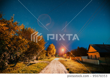 Night sky over street with houses in village. Night starry sky above village with bright stars and meteoric track trail. Glowing stars above summer nature 95078353