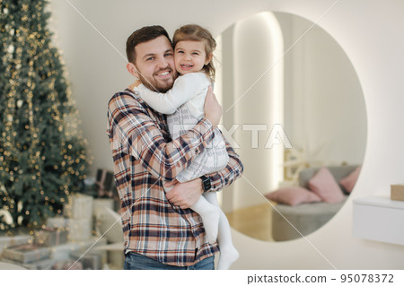 Adorable daughter with her dear father at home in gront of fit tree. Chrisrmas mood. Daughter hug father 95078372