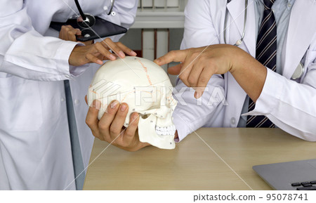 Young asian doctor in white gown and stethoscope asking for the professor advice about different part of skull. Working atmosphere in hospital. 95078741