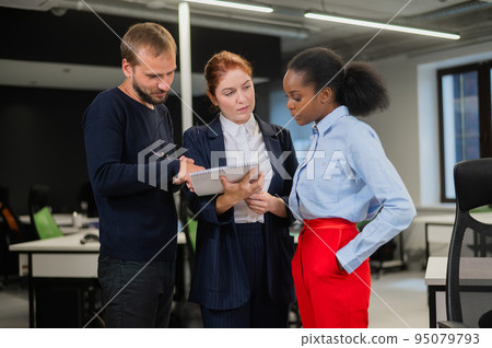 Colleagues discuss work. African young woman, caucasian man and red-haired caucasian woman communicate in the office.  95079793