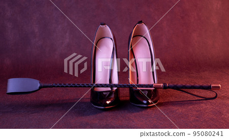 Black shiny high heel shoes and a whip on a dark background Black shiny high heel shoes and a whip on a dark background 95080241