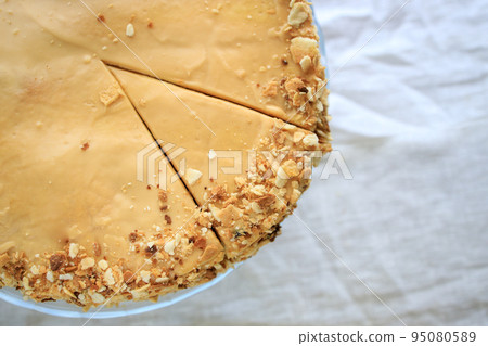 round napoleon cake, with caramel cream and a cut off piece, on a white background. copy space round napoleon cake, with caramel cream and a cut off piece, on a white background. copy space 95080589