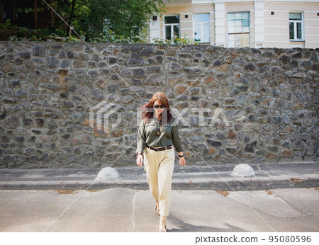 happy smiling young brunette woman in sunglasses walking along the city street 95080596