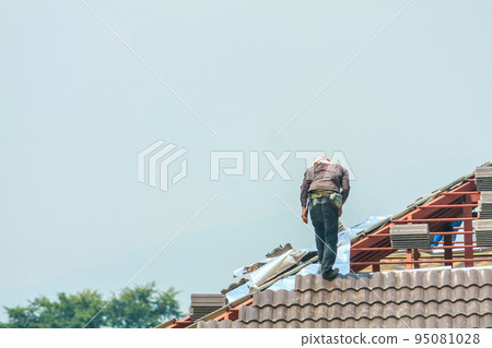 Construction roofer installing roof tiles at house building site 95081028