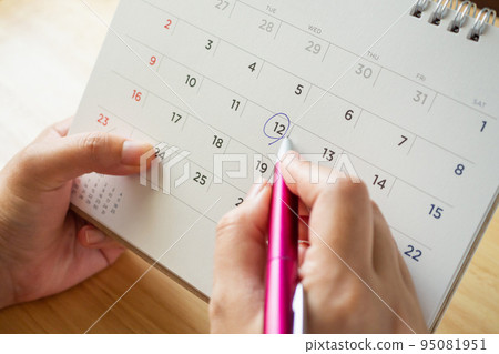 calendar page with female hand holding pen on desk table 95081951