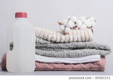 wool detergent in a bottle and stack of pullovers with cotton buds. special fabric softener for delicate textile and knitted apparel wool detergent in a bottle and stack of pullovers with cotton buds. special fabric softener for delicate textile and knitted apparel 95083151