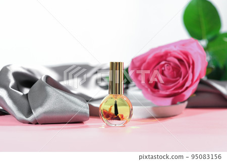 cuticle massage oil with rose petals infusion. pink rose flower next to a bottle of nail care oil, hans and nails beauty care, skin moisturizing and nourishing, spa manicure concept. 95083156