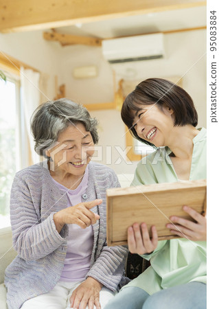 Senior woman looking at photos with grandchildren Senior woman looking at photos with grandchildren 95083884