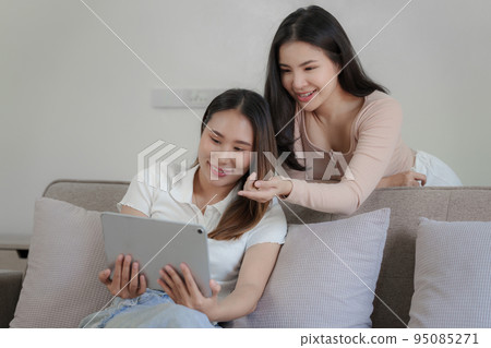 Two asian women having nice lively conversation in living room on sofa in cozy interior Two asian women having nice lively conversation in living room on sofa in cozy interior 95085271