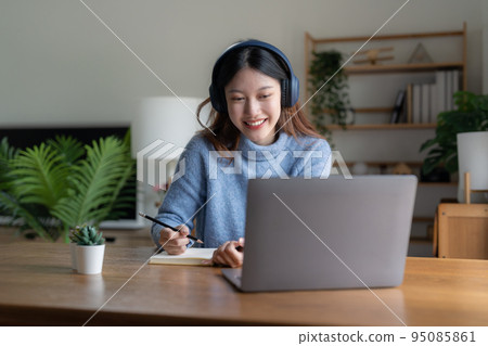Smiling girl student wear headphone study online with teacher, happy young asian woman learn language listen lecture watch webinar write notes look at laptop sit in cafe, distant education Smiling girl student wear headphone study online with teacher, happy young asian woman learn language listen lecture watch webinar write notes look at laptop sit in cafe, distant education 95085861