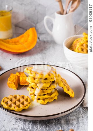 A stack of pumpkin waffles with sweet sauce on a plate on the table. Homemade baking. Vertical view A stack of pumpkin waffles with sweet sauce on a plate on the table. Homemade baking. Vertical view 95086117
