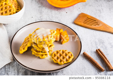 A stack of pumpkin waffles with sweet sauce on a plate on the table. Homemade baking. 95086118