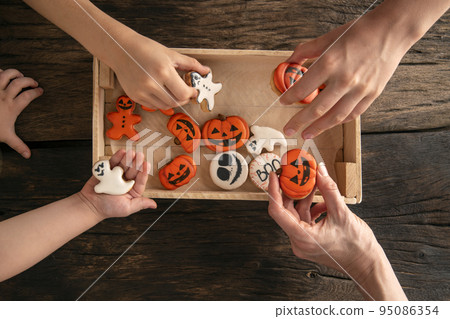 Funny delicious ginger cookies for Halloween on the table. Hands take cookies. Halloween gingerbread cookies in box Funny delicious ginger cookies for Halloween on the table. Hands take cookies. Halloween gingerbread cookies in box 95086354