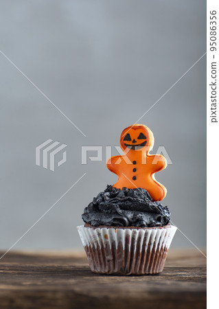 Festive Halloween cupcakes decorated with black cream and gingerbread man on grey background. Delicious halloween party muffins Festive Halloween cupcakes decorated with black cream and gingerbread man on grey background. Delicious halloween party muffins 95086356