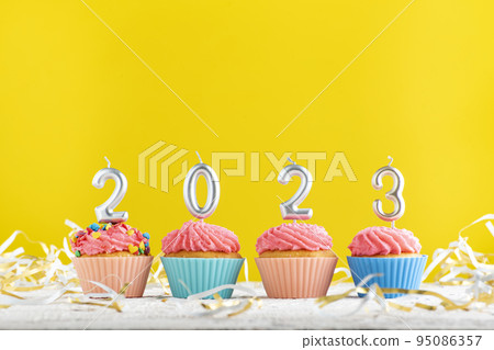 Bright Christmas theme with candles in the shape of numbers 2023 on cupcakes on yellow background. Copy space. 95086357