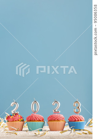 Festive cupcakes and candles in form of numbers 2023 on blue background. Concept of New year. Vertical frame Festive cupcakes and candles in form of numbers 2023 on blue background. Concept of New year. Vertical frame 95086358