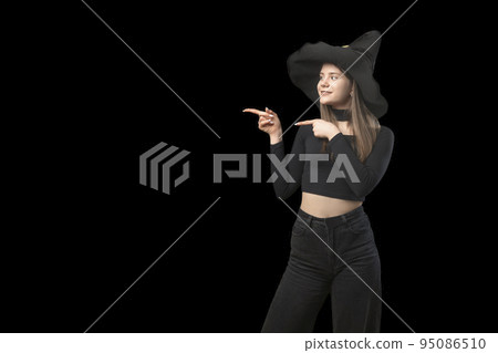 Young woman witch in pointed hat point her finger. Copy space. Isolated on black background. Place for your text. 95086510