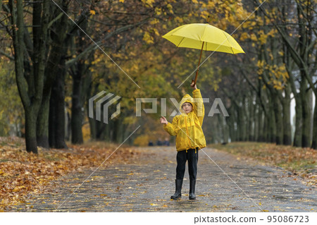 Child in yellow raincoat walks in an autumn park with large yellow umbrella in his hands. Rainy day 95086723