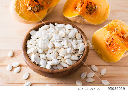 Roasted unpeeled pumpkin seeds in a plate and slices of pumpkin on a wooden table 95086939