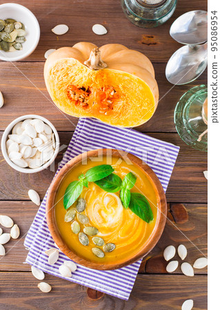 Top view of Vegetarian autumn pumpkin puree soup with seeds, basil and cream in a wooden plate on the table. Vertical view 95086954