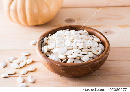 Roasted pumpkin seeds in a plate and pumpkin on a wooden table Roasted pumpkin seeds in a plate and pumpkin on a wooden table 95086977