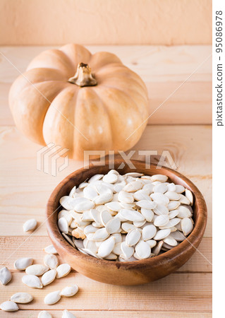 Roasted pumpkin seeds in a plate and pumpkin on a wooden table. Vertical view 95086978
