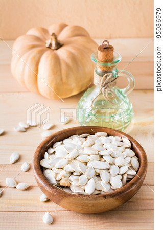 Roasted pumpkin seeds in a plate, oil in a bottle and pumpkin on a wooden table Roasted pumpkin seeds in a plate, oil in a bottle and pumpkin on a wooden table 95086979