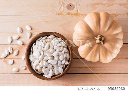 Roasted pumpkin seeds in a plate and pumpkin on a wooden table. Top view Roasted pumpkin seeds in a plate and pumpkin on a wooden table. Top view 95086980