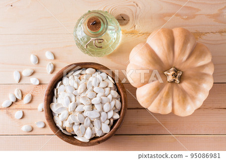 Roasted pumpkin seeds in a plate, oil in a bottle and pumpkin on a wooden table. Top view Roasted pumpkin seeds in a plate, oil in a bottle and pumpkin on a wooden table. Top view 95086981
