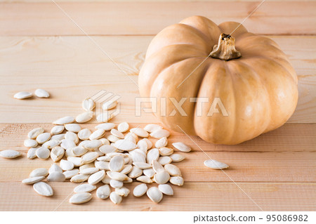 Roasted unpeeled pumpkin seeds and pumpkin on a wooden table Roasted unpeeled pumpkin seeds and pumpkin on a wooden table 95086982