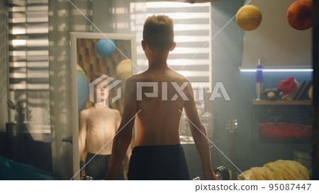 School boy do dumbbells curls in front of the mirror in his room nude upper body School boy do dumbbells curls in front of the mirror in his room nude upper body 95087447