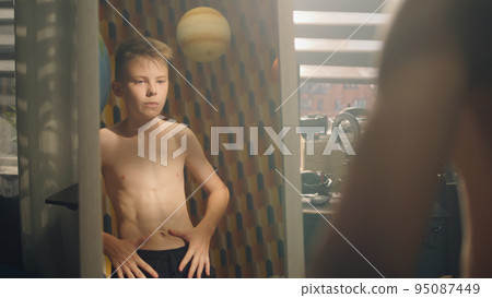 Muscular young boy examines his body infront of the mirror after weight training 95087449