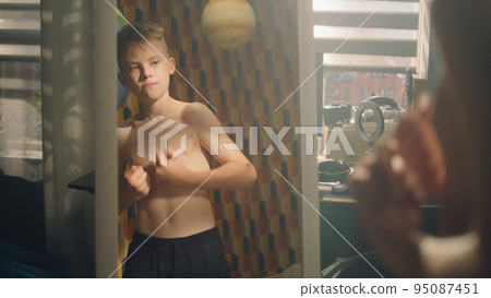 Muscular young boy examines his body infront of the mirror after weight training 95087451