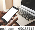 Smartphone white screen mockup on a man hand on laptop computer black keyboard white phone screen mock-up on a desk office with copy space. The concept for using an advertising banner text. 95088312