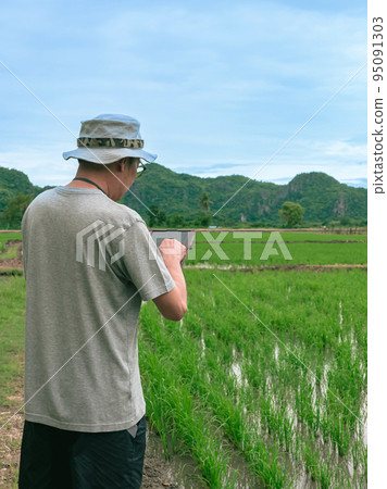 Asian male farmer using tablet for research leaves of rice in organic farm field. Agriculturist check the growing rice production in rice paddy field by using tablet. Agricultural technology Concept. Asian male farmer using tablet for research leaves of rice in organic farm field. Agriculturist check the growing rice production in rice paddy field by using tablet. Agricultural technology Concept. 95091303